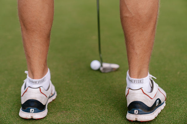 A golfer standing over a putt in white Immerse ankle socks and golf shoes