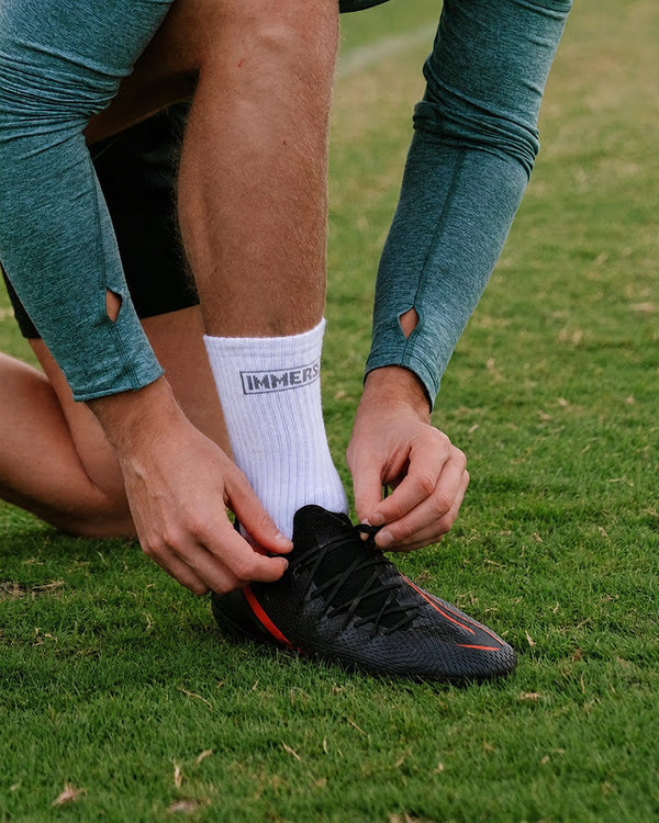 Lacing a black boot over a white Immerse crew grip sock on the pitch