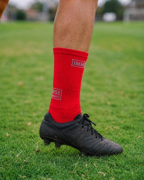 Immerse GRIP Crew Red worn in a black football boot on grass