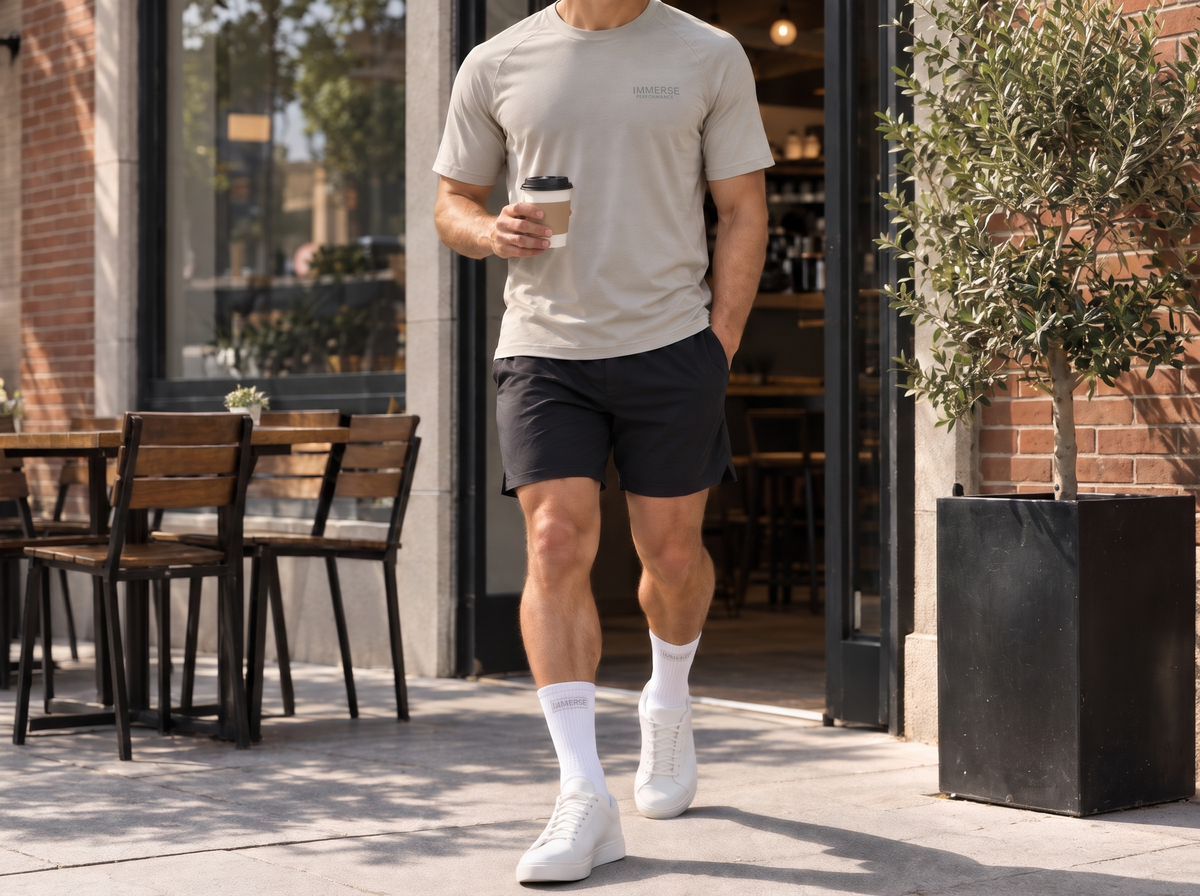 A man walks out of a cafe with a coffee in the Immerse stone tee and white Immerse crew socks